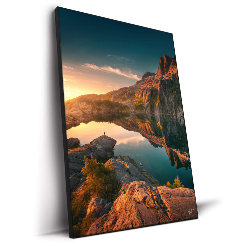 Lone figure by a pristine mountain lake in British Columbia, with mirrored reflections of rugged cliffs.