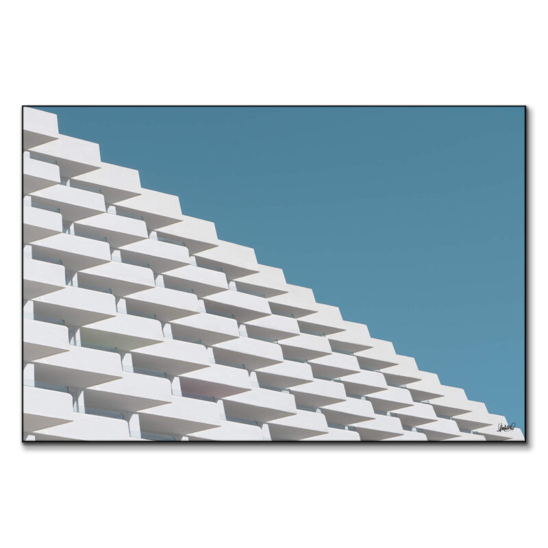 Building facade with white angled balconies cascading against a blue sky.
