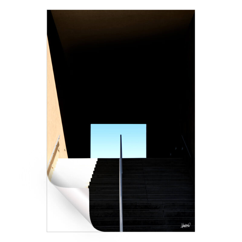 Dark stairway leading into darkness with a bright opening and clear blue sky.