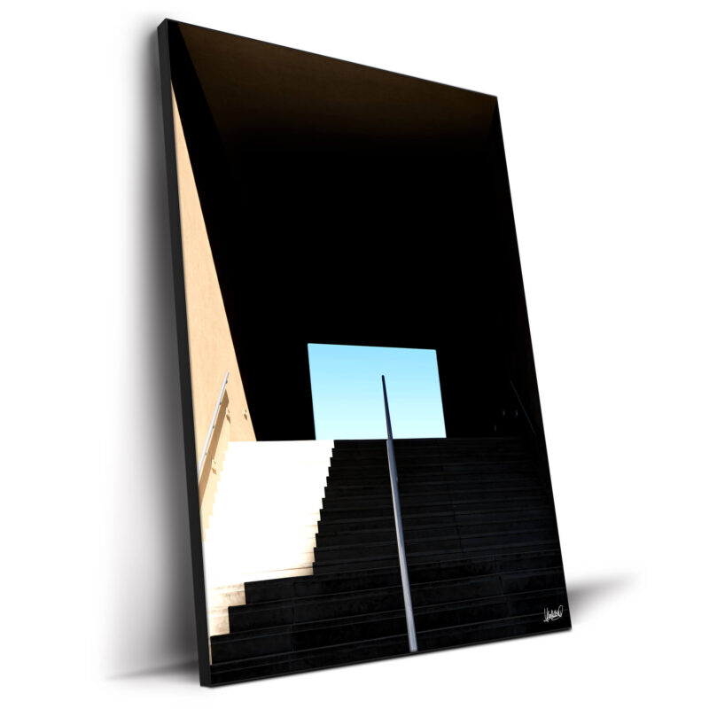 Staircase leading into darkness with a bright opening and clear blue sky, highlighting strong lines and shadows.