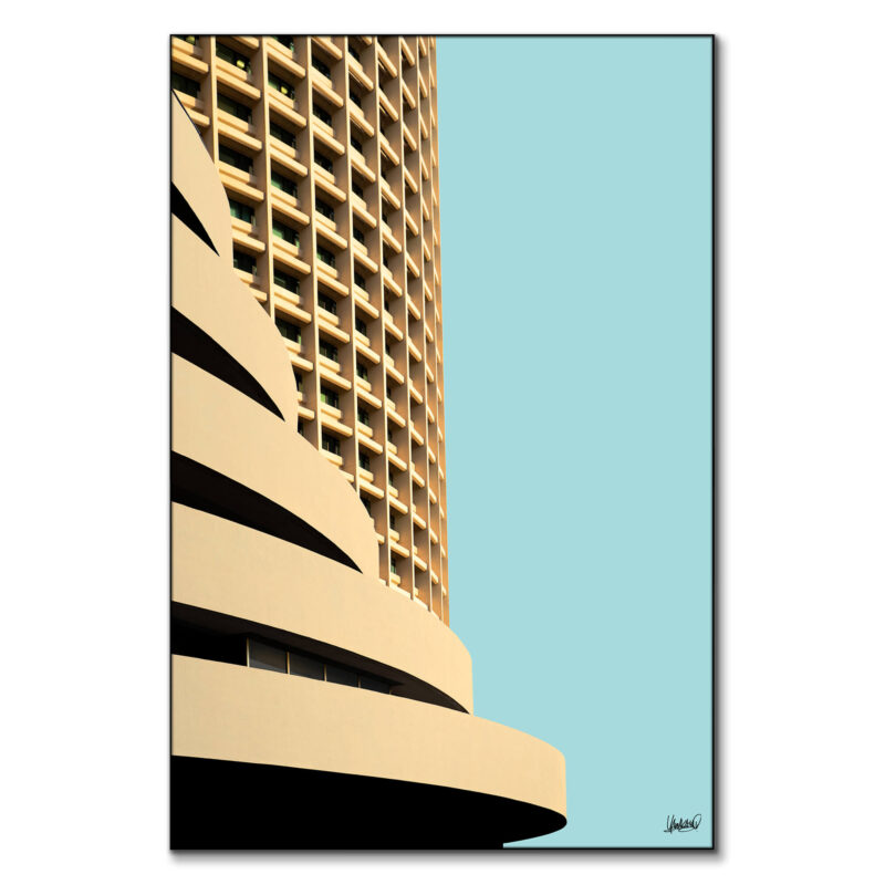 Tan curved high-rise building with repetitive windows against a light blue sky.