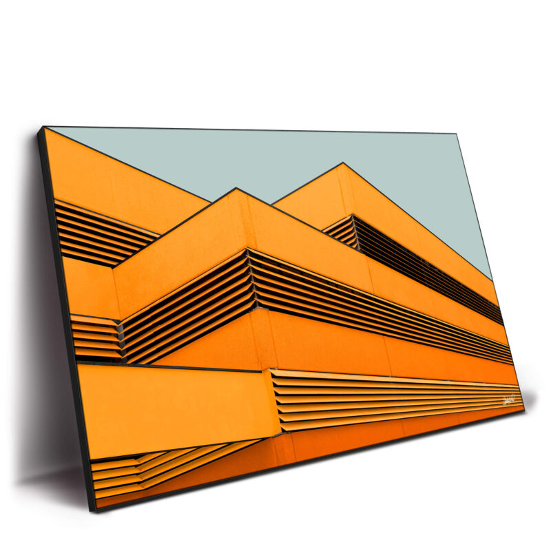Geometric building facade with orange panels and black slats in a pattern against a gray-blue background.