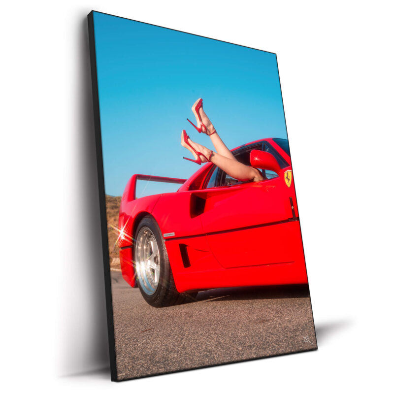 Red Ferrari with legs in red high heels playfully extending from the window under a clear blue sky.