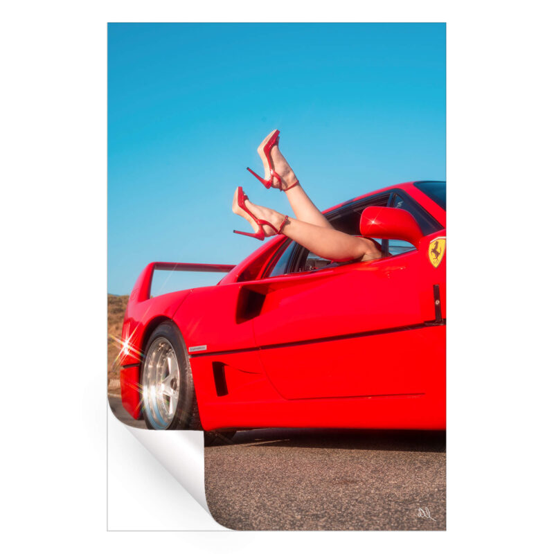 Red sports car with legs in red high heels playfully extending from the window under a clear blue sky.