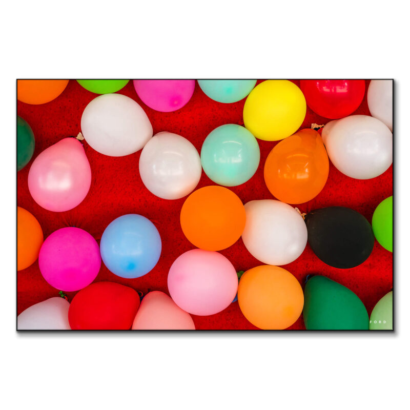 Assorted colorful party balloons scattered on a vibrant red background, creating a festive and playful atmosphere.