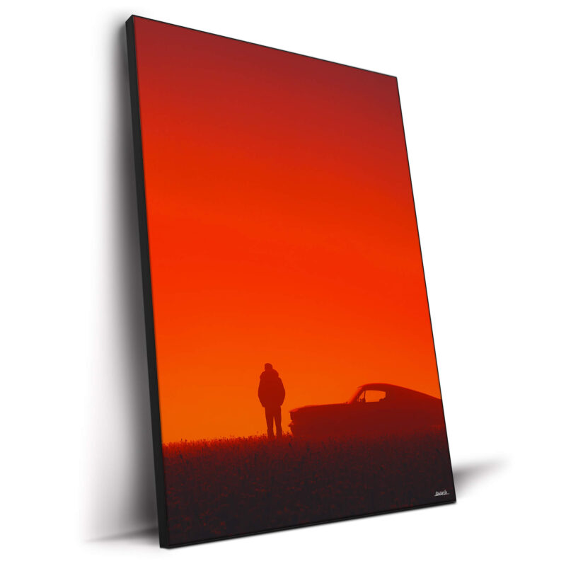 A silhouette of a man standing next to a vintage car against a red sunset backdrop.