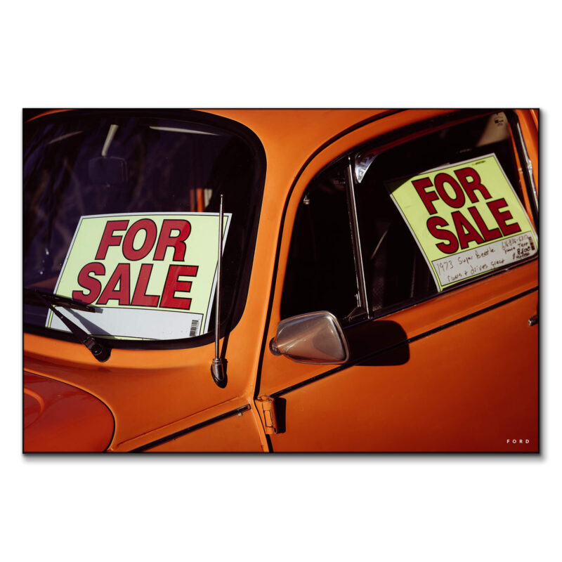 Vintage orange beetle car with 'For Sale' signs in the windows.