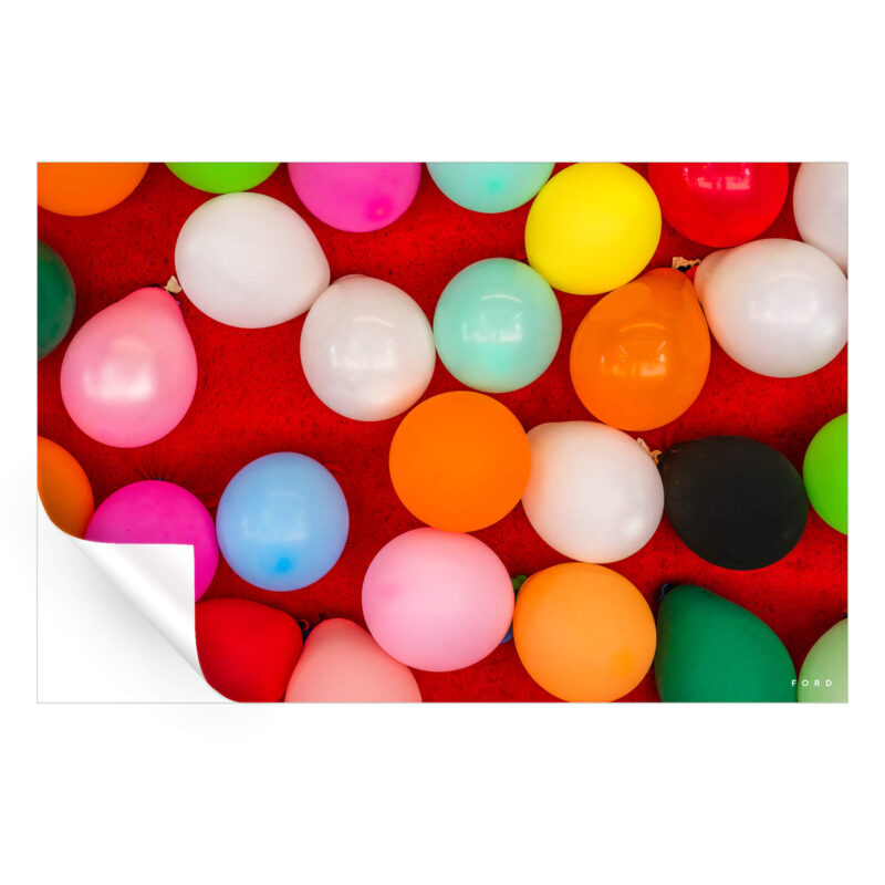 Assorted colorful party balloons scattered on a vibrant red background, creating a festive and playful atmosphere.