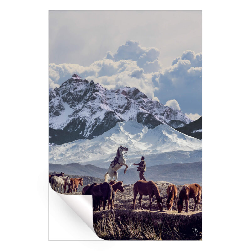 Cowboy with a horse in front of snow-capped mountains, surrounded by grazing horses in a tranquil landscape.