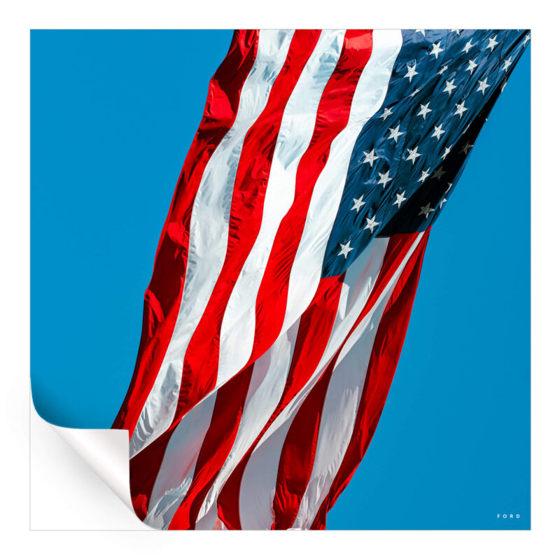Photograph of the American flag waving in the wind against a clear blue sky.
