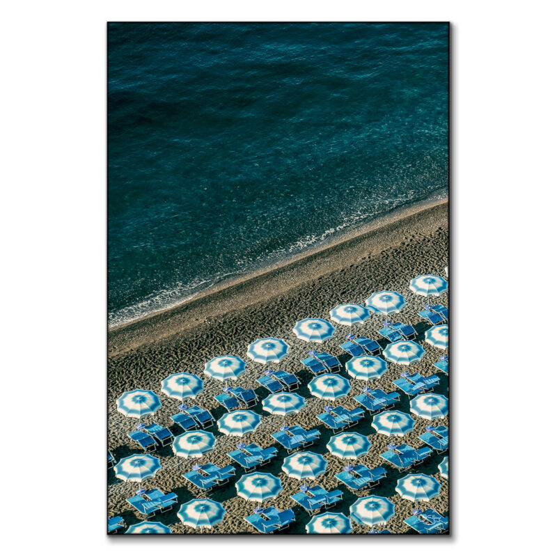 Overhead view of blue beach umbrellas on a sandy beach next to the ocean.