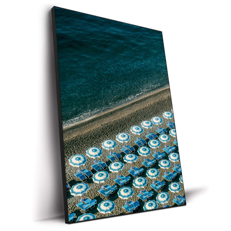 Overhead view of blue beach umbrellas on a sandy beach next to the ocean.
