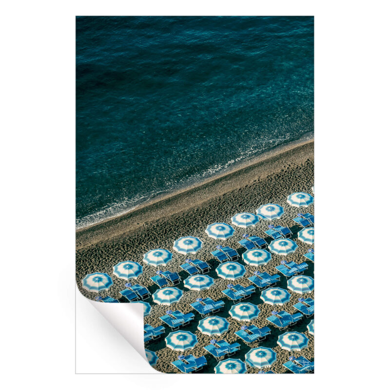 Overhead view of blue beach umbrellas on a sandy beach next to the ocean.