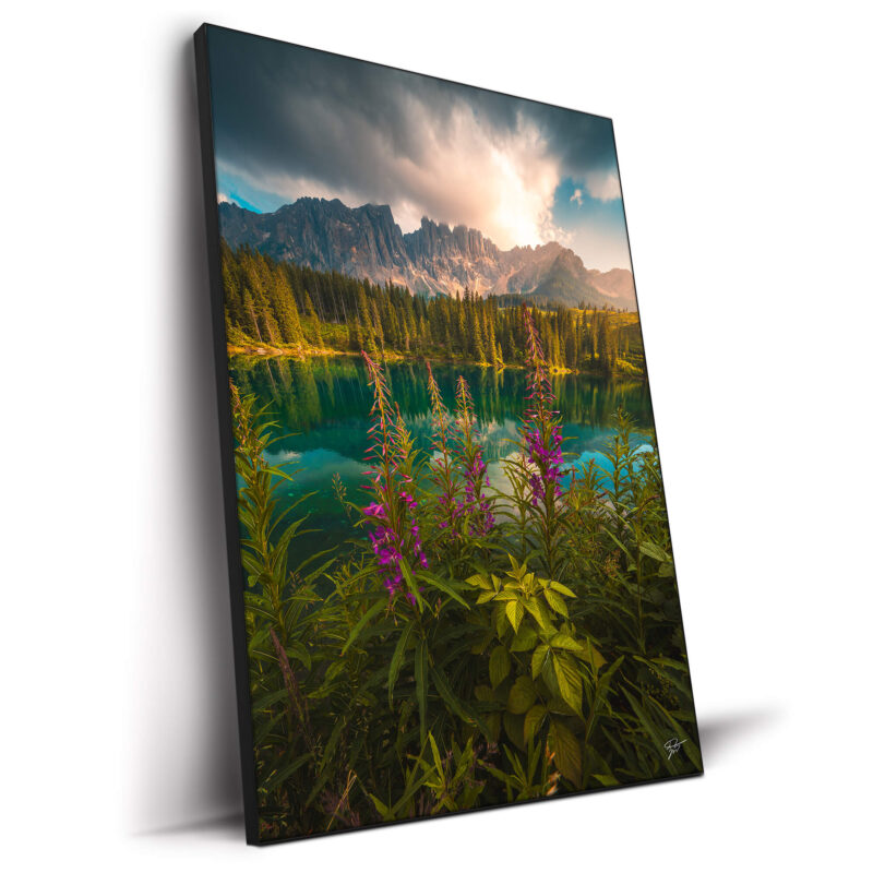 Serene landscape with mountain lake, flowers, and lush green foliage under a bright sky.