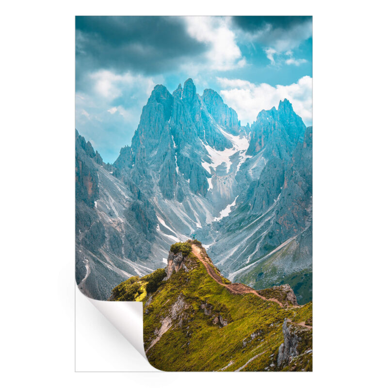 A person standing on a mountain peak, overlooking a vast and rugged landscape of valleys and peaks.