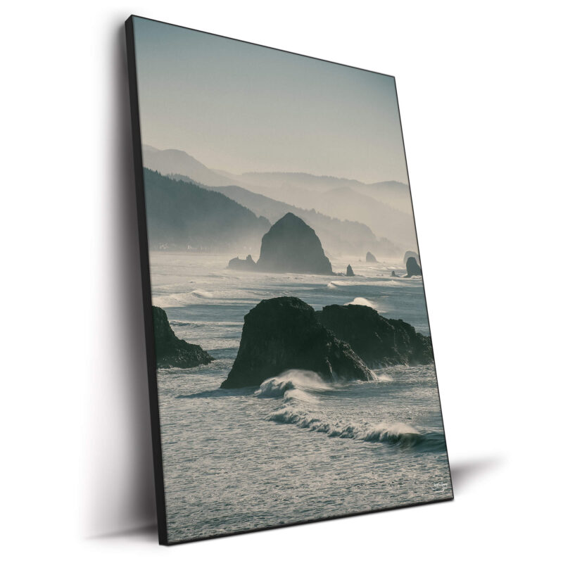 A misty coastal landscape featuring rugged sea stacks emerging from ocean waves, with rolling hills in the background.